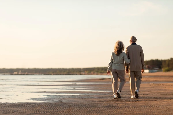 Couple senior marchant main dans la main au bord de la mer au coucher du soleil